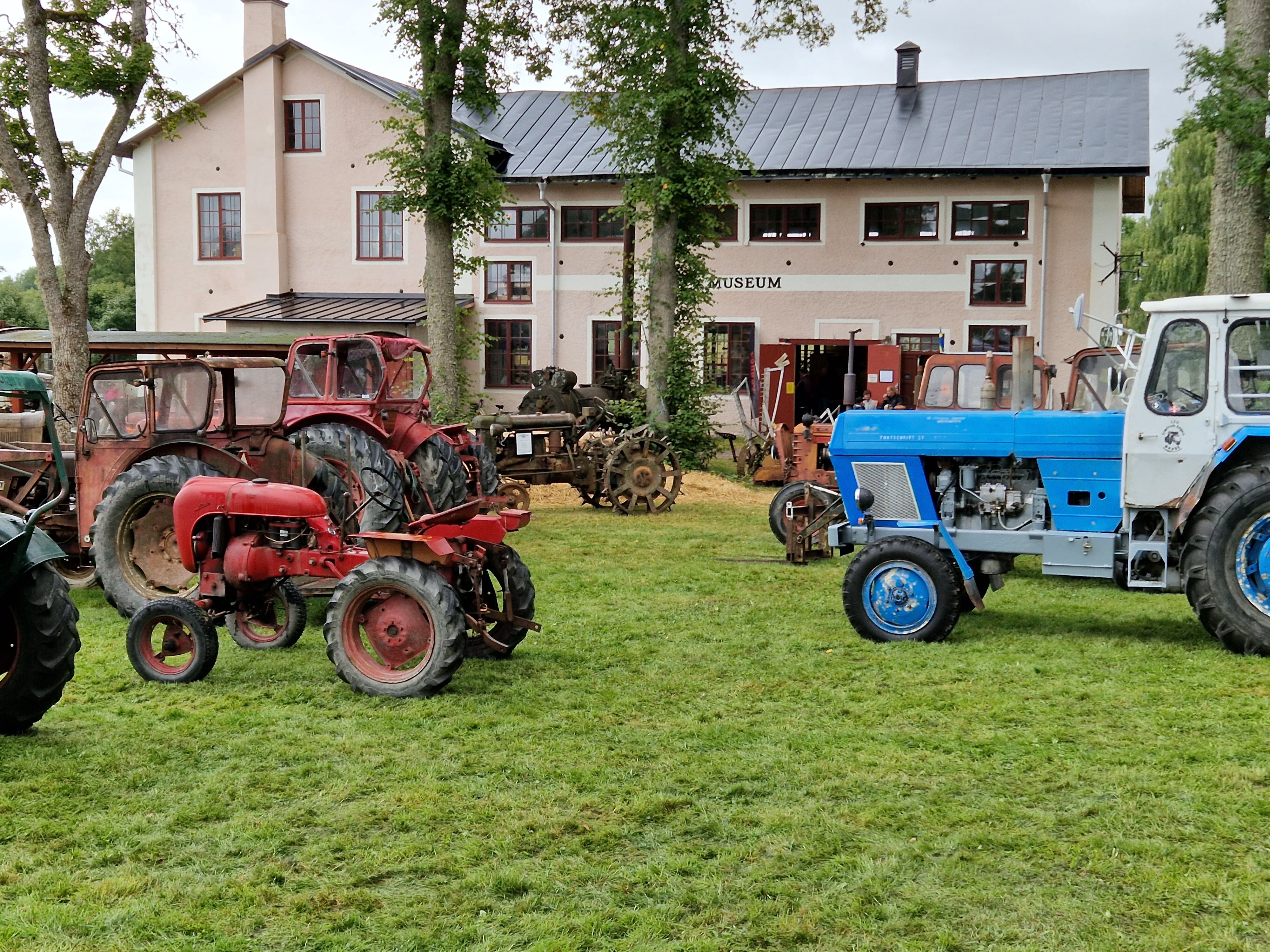 Bilden visar gamla traktorer stående i gräset utanför ett hus som är museum i Jäders bruk.