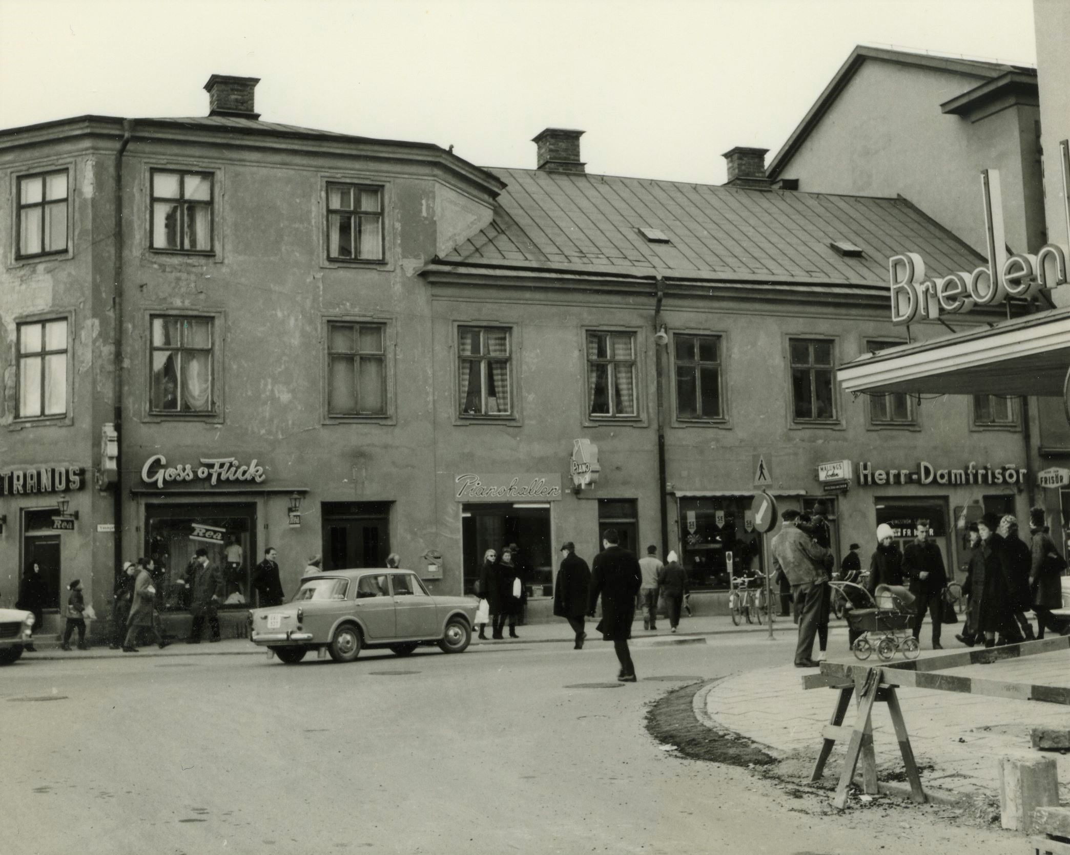 Gatubild med en livlig gata med människor, butiker och bilar på 1960-talet.
