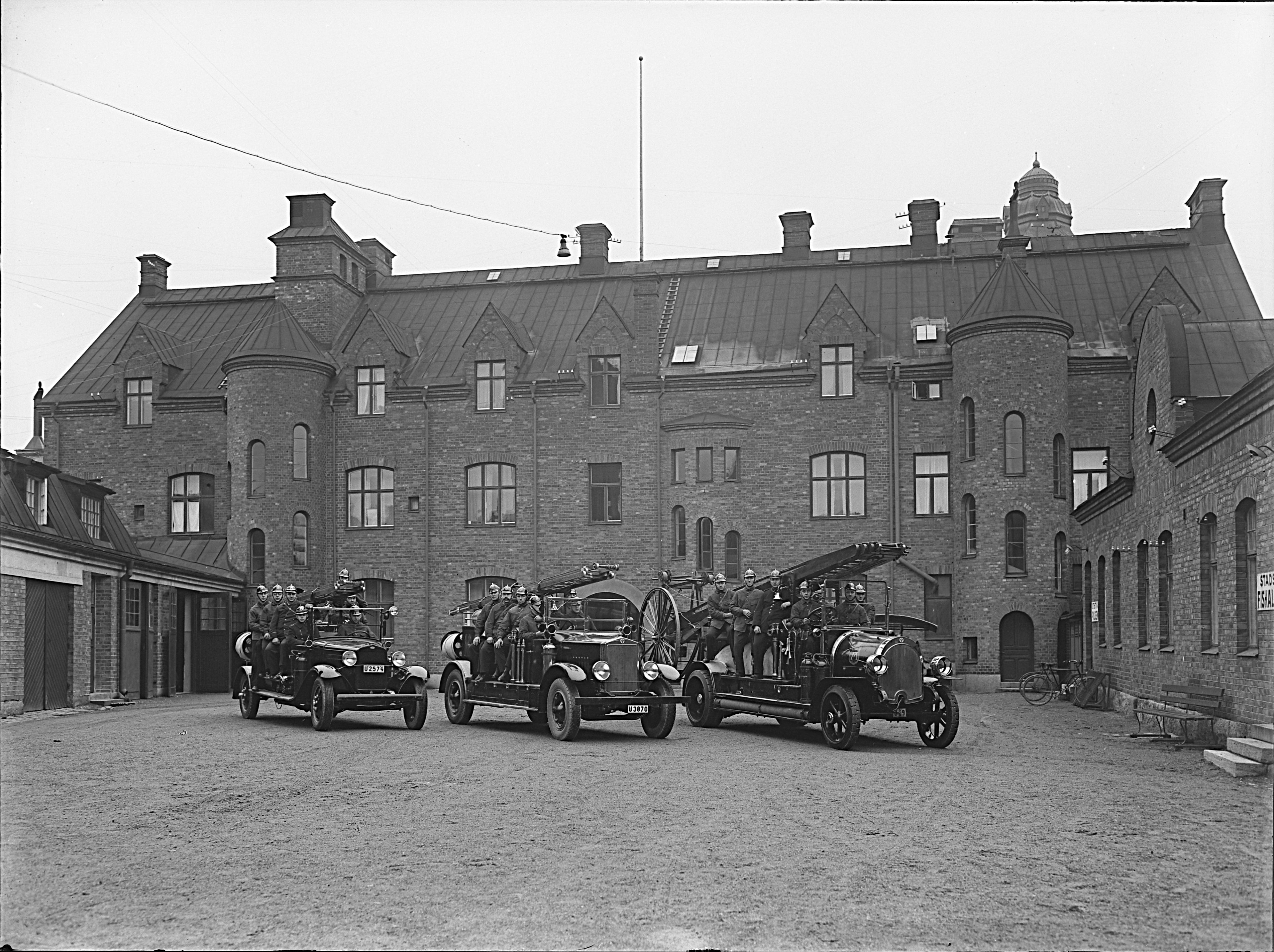 Brandmän i bilar på brandstationens gård.
