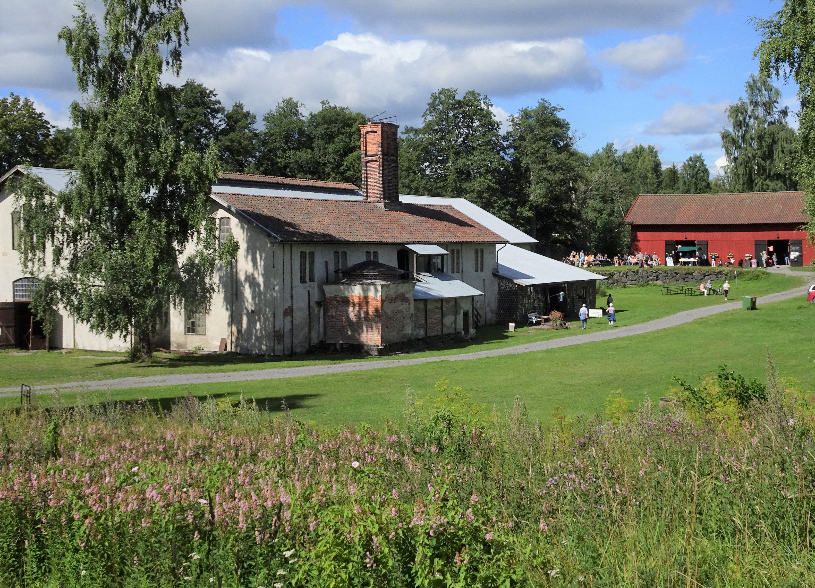 Karmansbo bruk. Bilden visar smedjan till vänster och det gamla kolhuset till höger. Där finns servering och man ser människor vid borden.