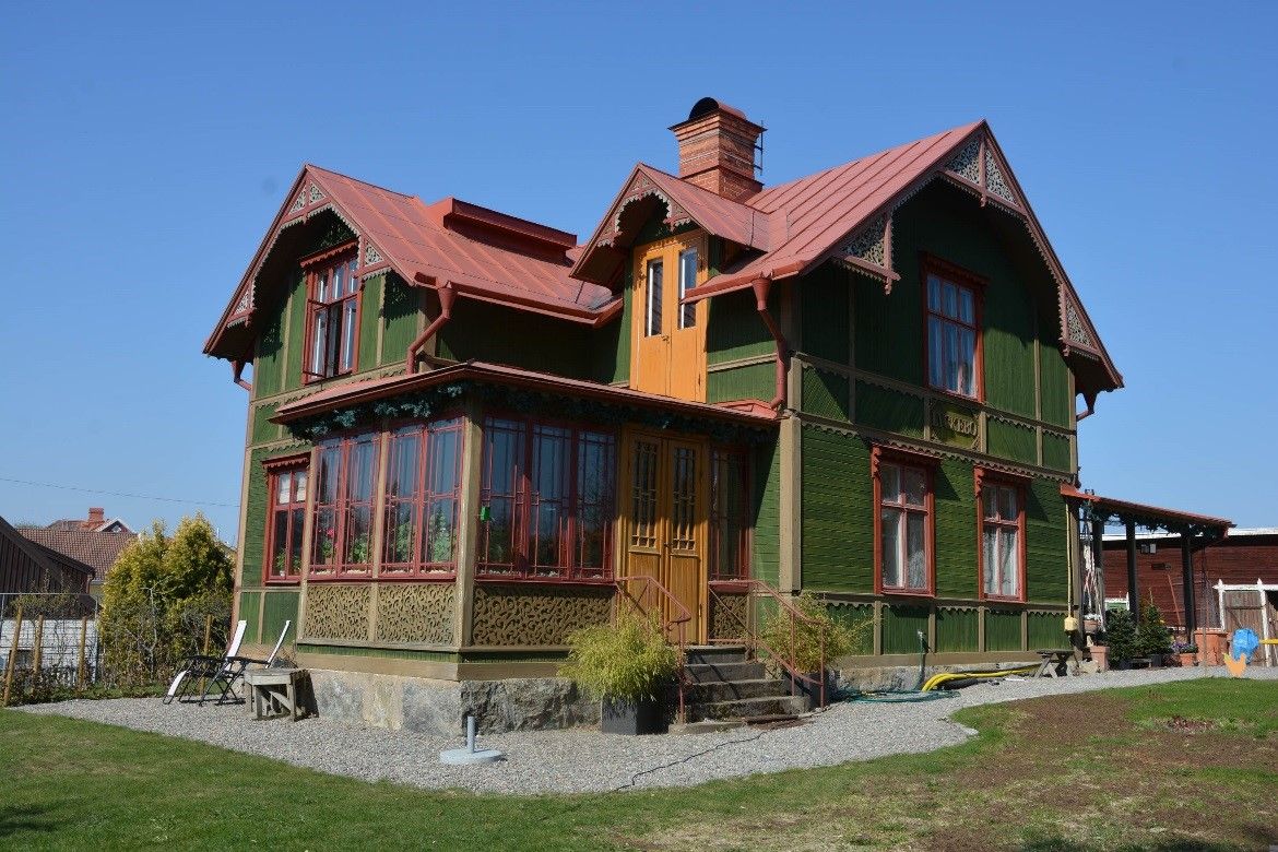 Grönt trähus med rött tak och glasveranda.