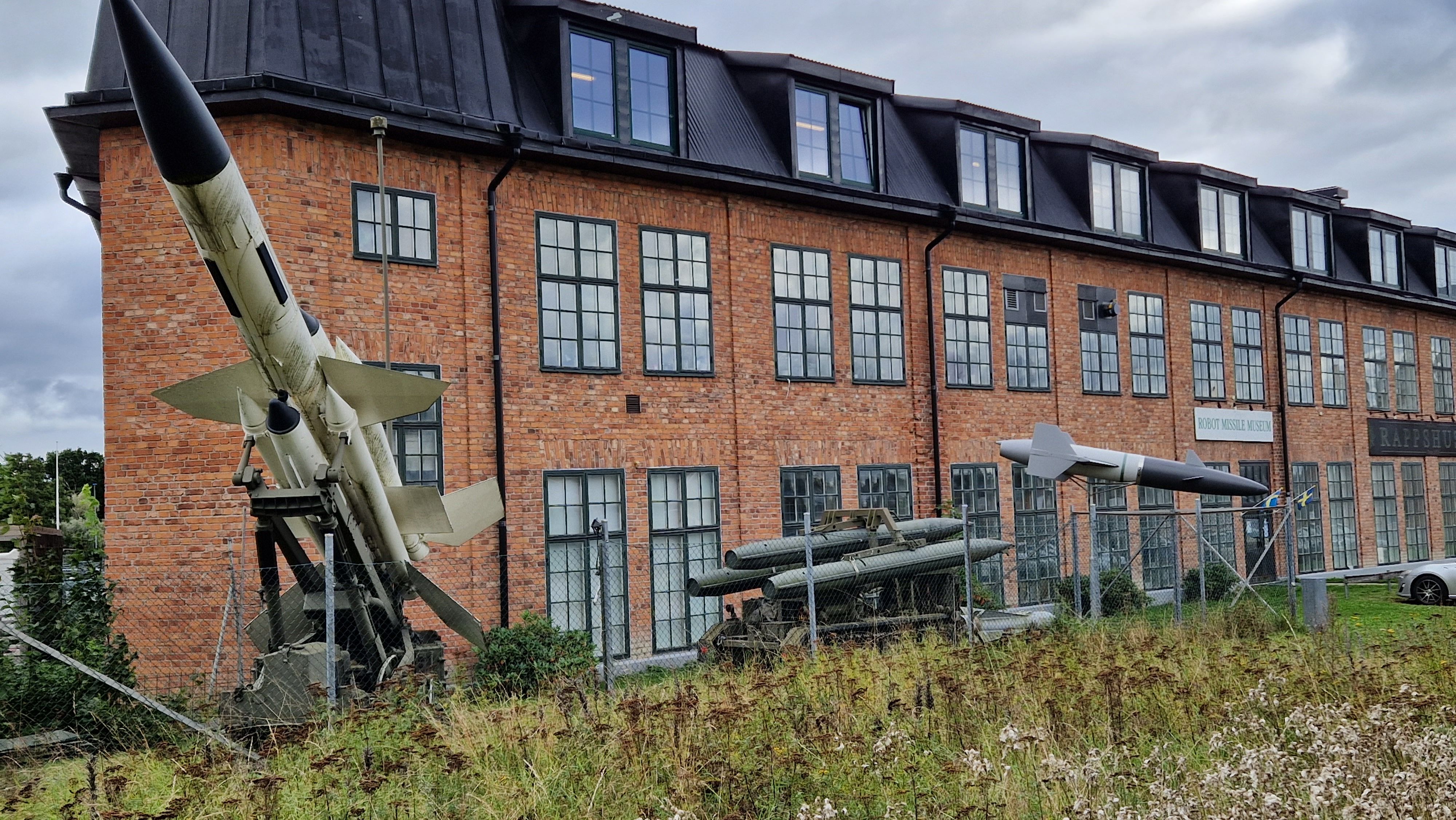 Bilden visar byggnaden med Arboga Robotmuseum. Framför byggnaden finns robotar som är självgående flygande projektiler för bekämpning av militära mål.