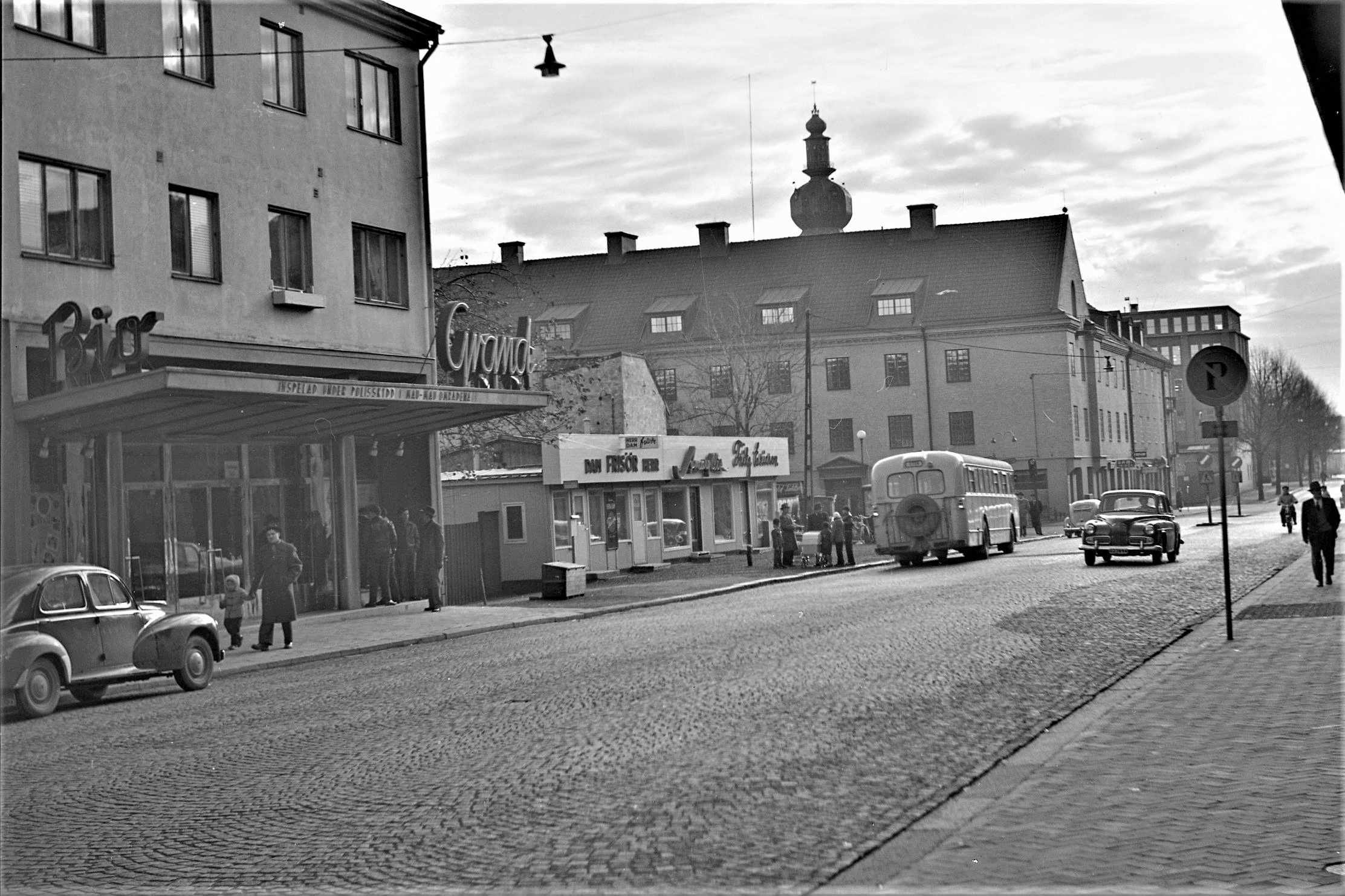 En gatuvy med bilar, buss, biograf och människor.