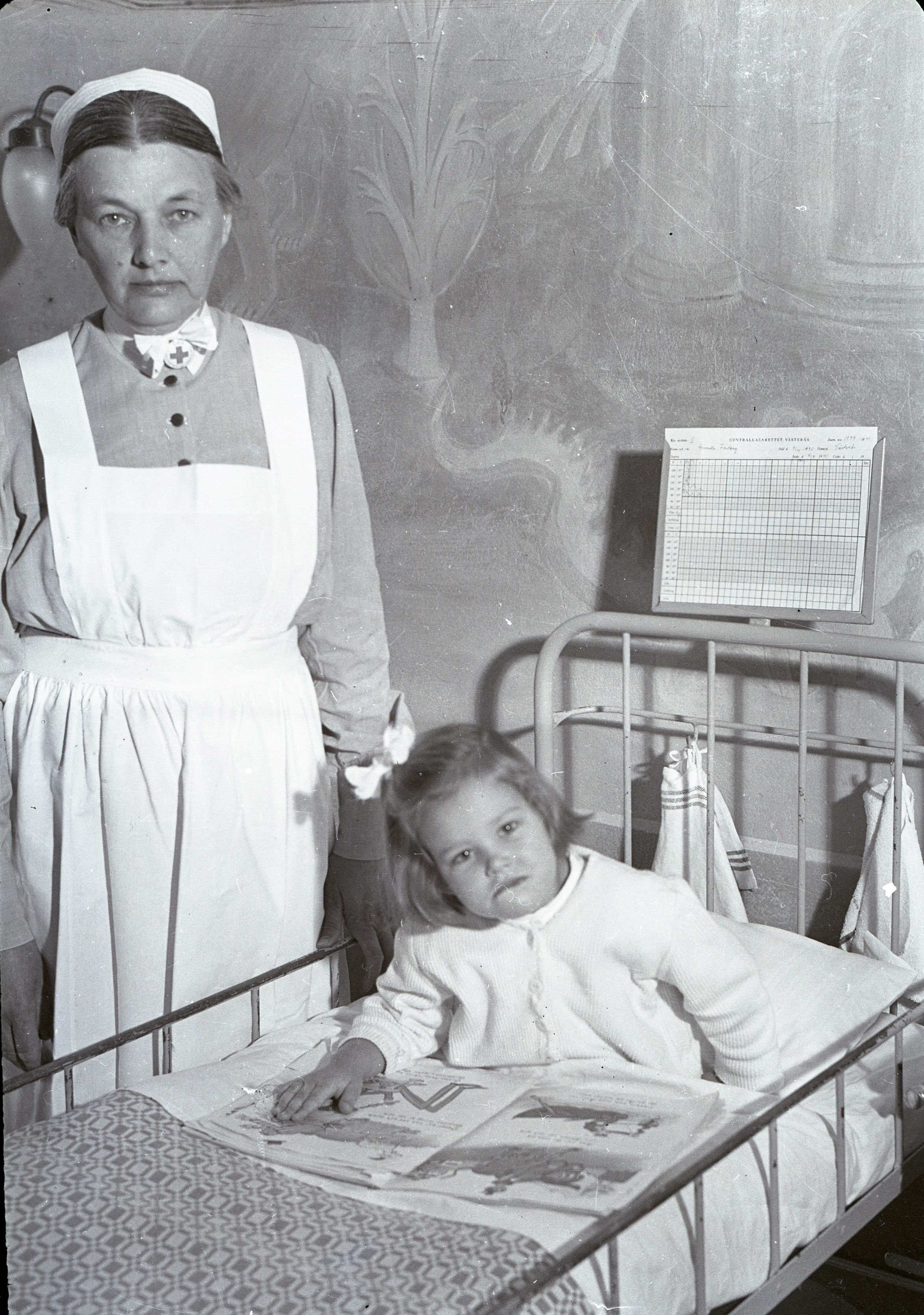 Svartvit foto med en flicka som ligger i en säng. Bredvid henne står en sjuksköterska