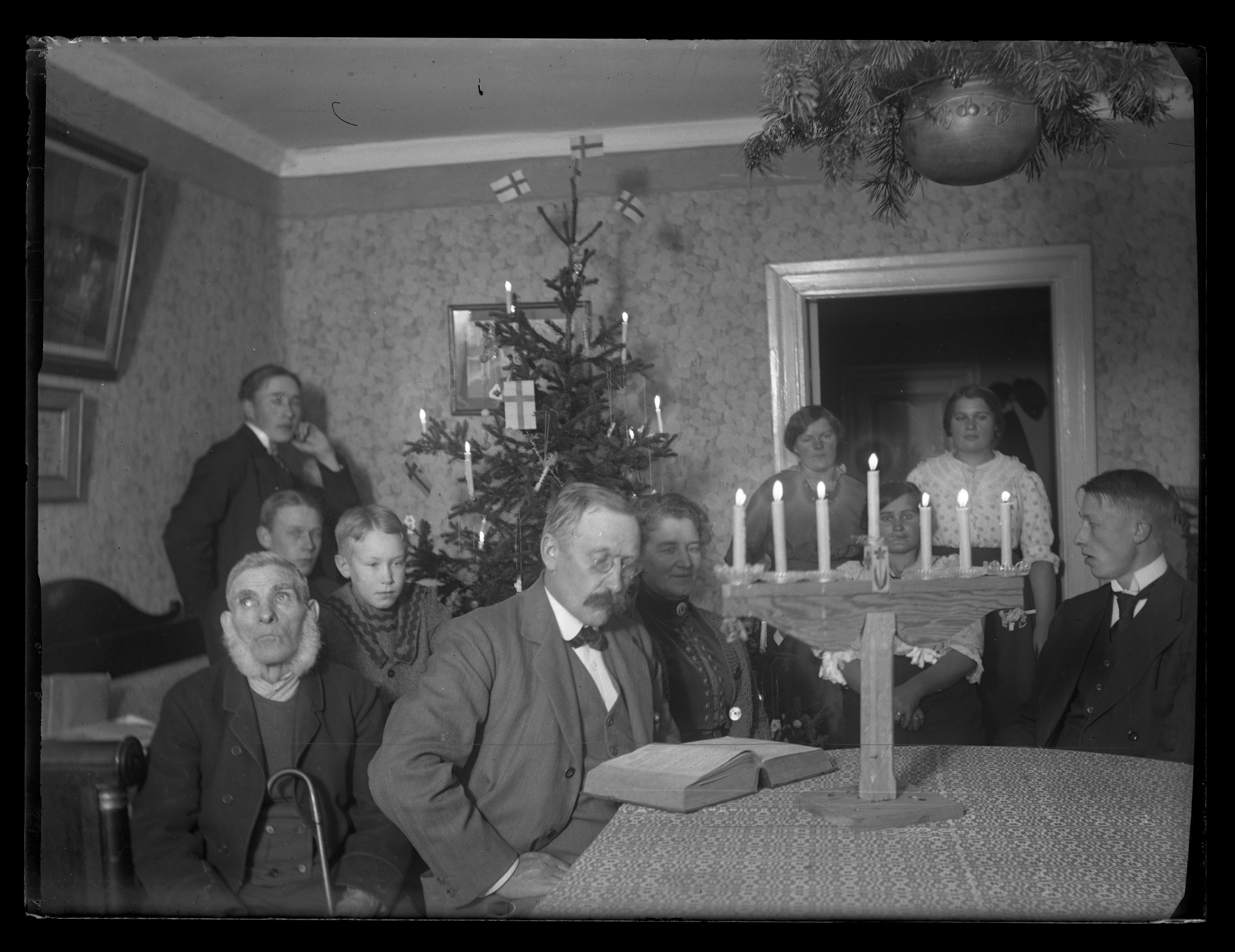 Svartvit foto på en familj sittandes vid ett bord, där en man sitter och läser i en bibel