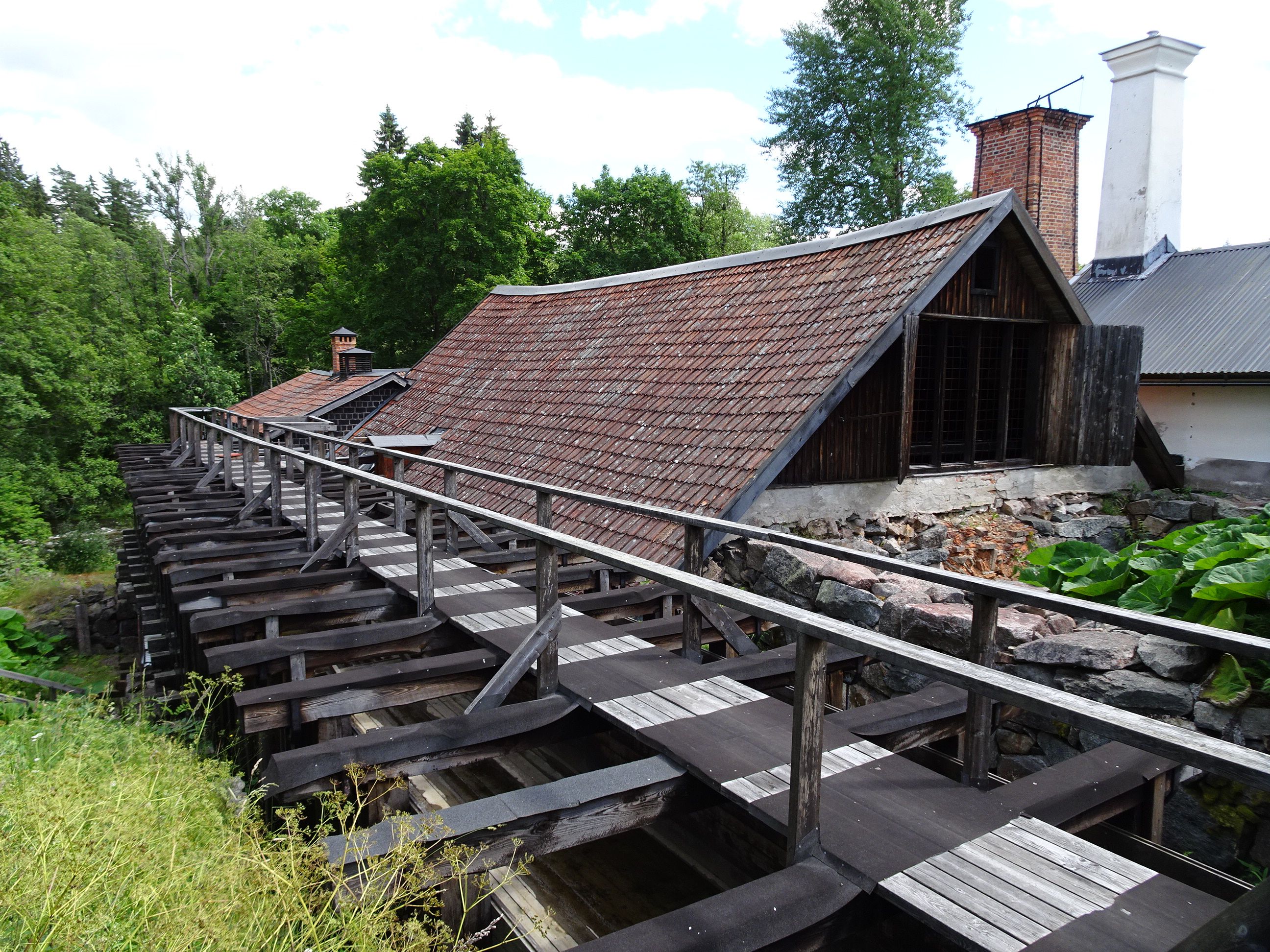 Bilden visar taket på smedjan och en plankgång ovanpå en träkonstruktion som leder vatten från kanalen till vattenhjulen.