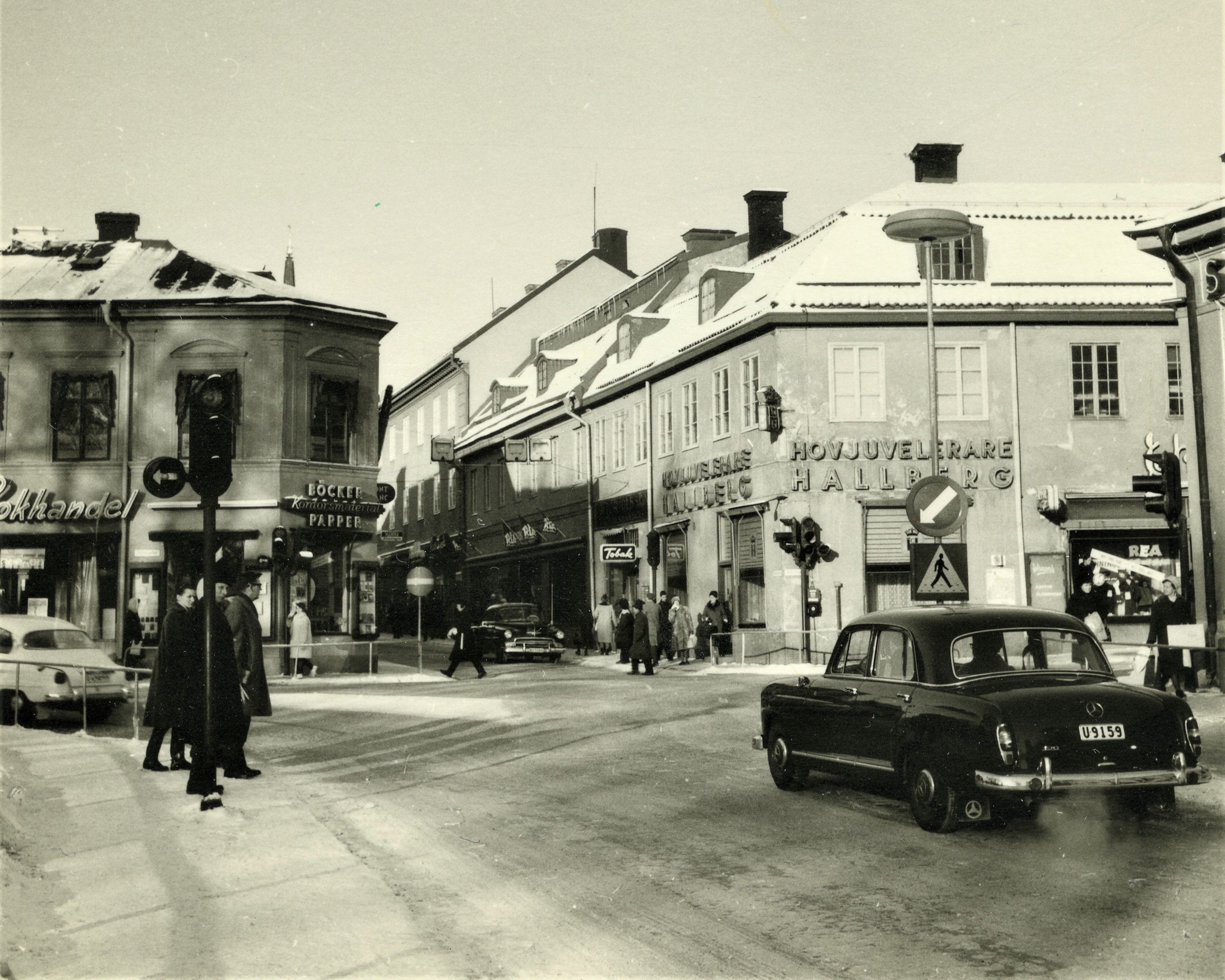 Livlig gata med människor, bilar och butiker. Ca 1960-talet.