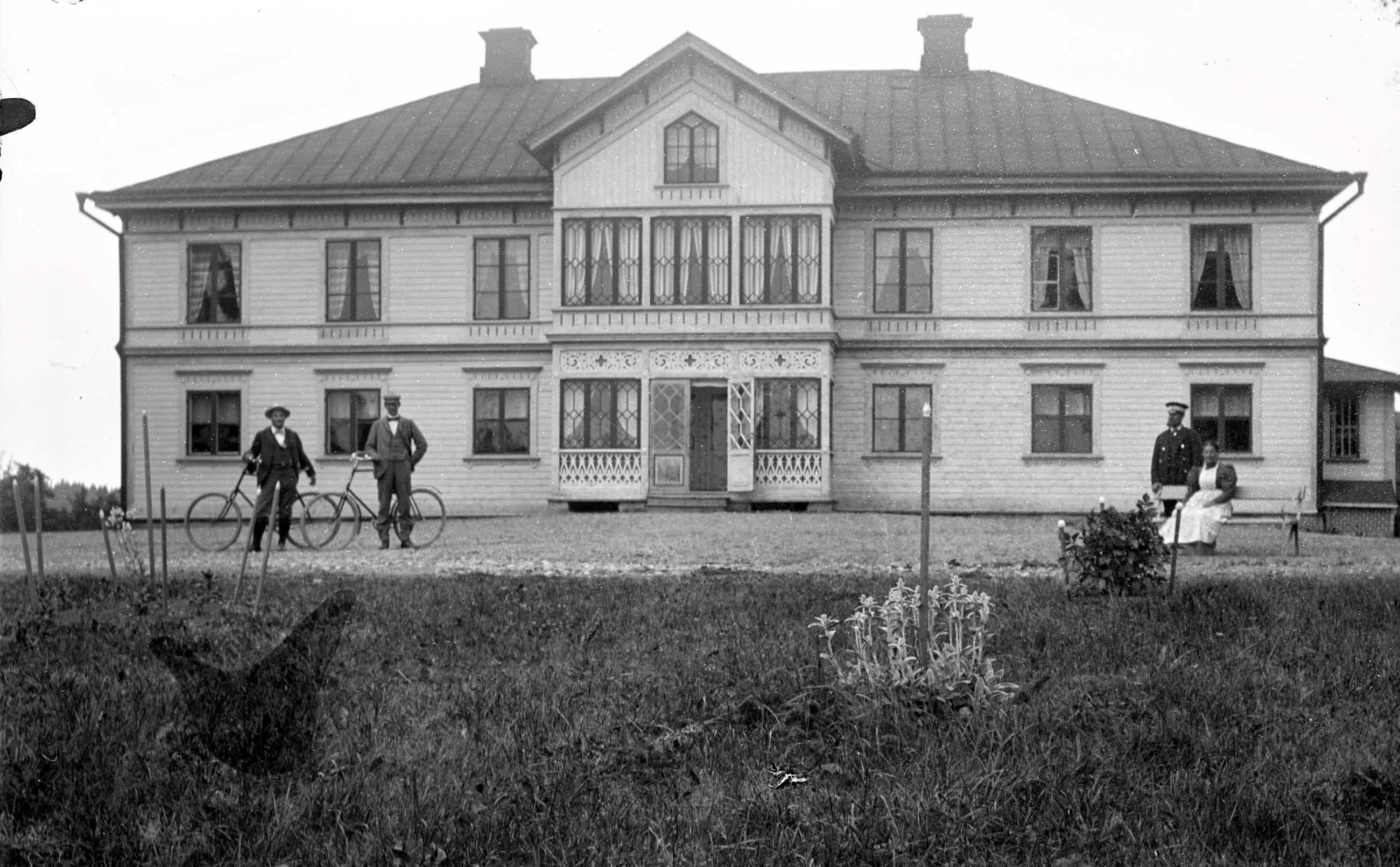Några människor, bland annat två män med cyklar framför en herrgårdsbyggnad.