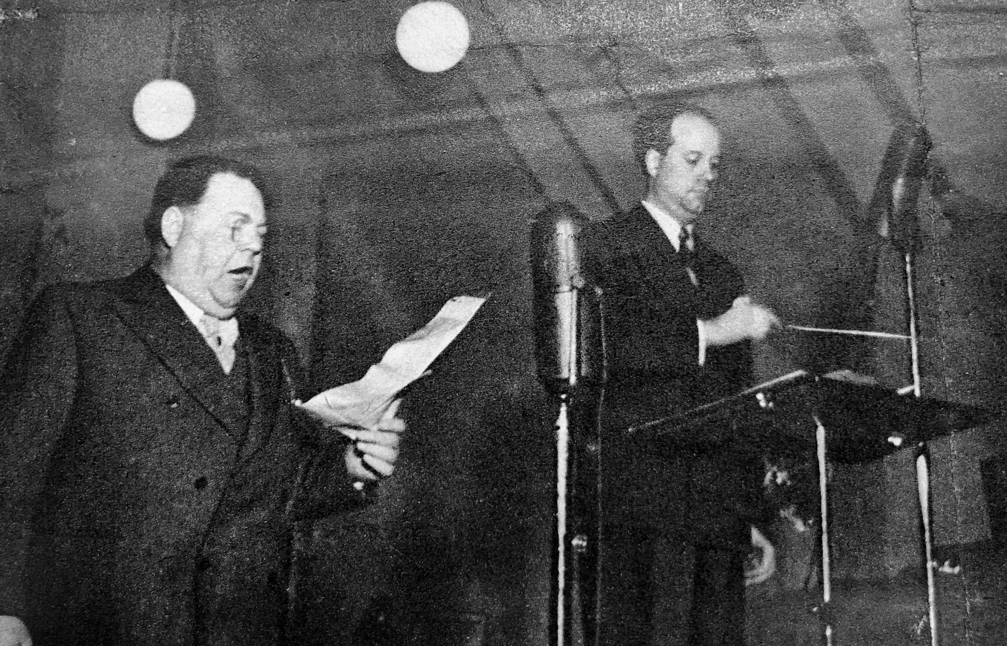 Sune Waldimir håller i taktpinnen medan Edvard Persson ser ner i ett papper och sjunger.