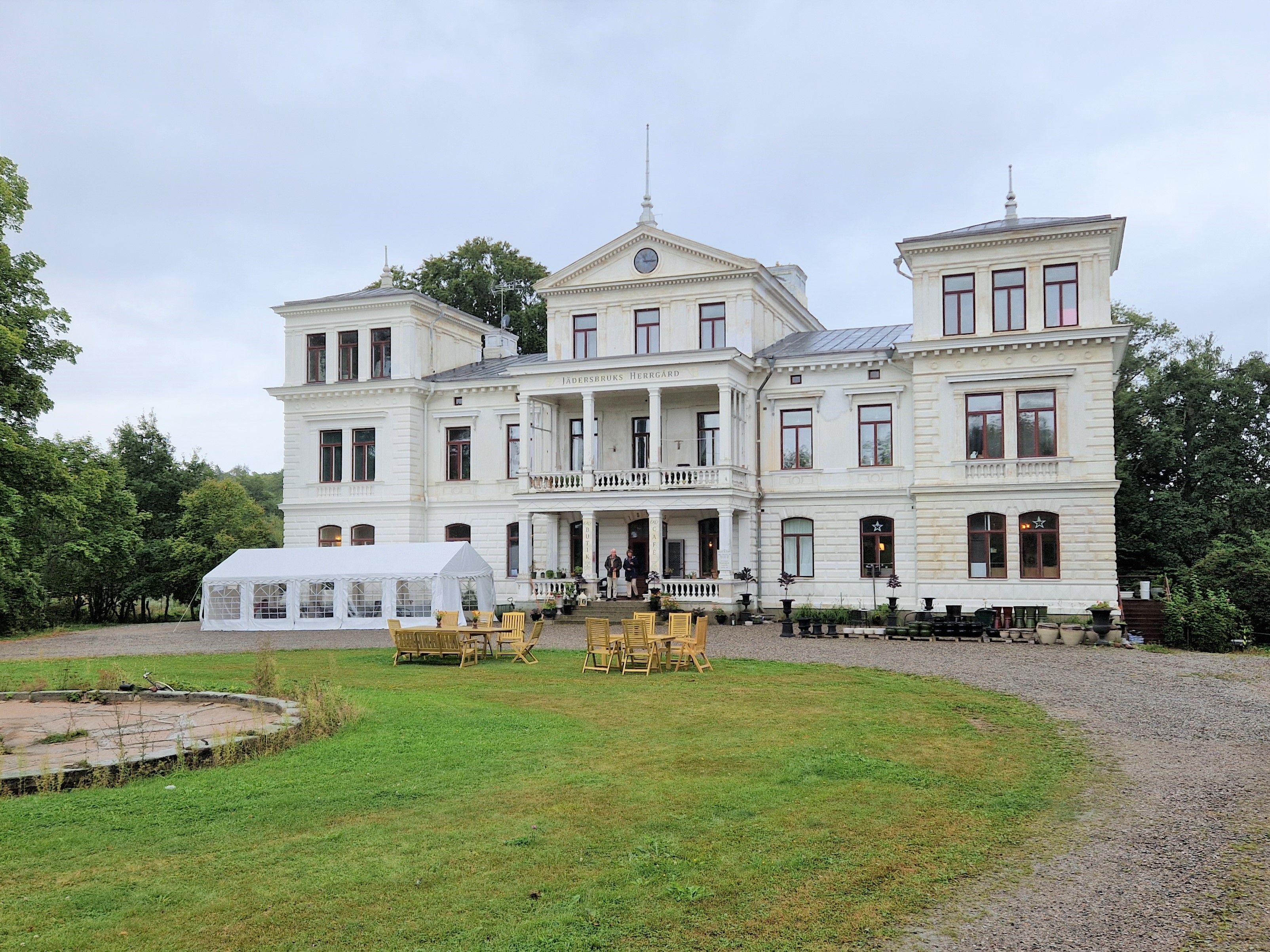 Bilden visar en vit herrgård med tre torn. Herrgården tillhör Jäders bruk. Gräsmatta framför.