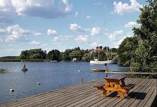 Vy över en sjöstrand från en träbrygga. En båt syns längre bort.